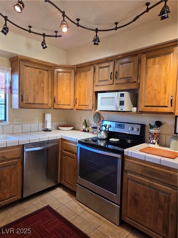 Kitchen with tile counters, brown cabinetry, dishw