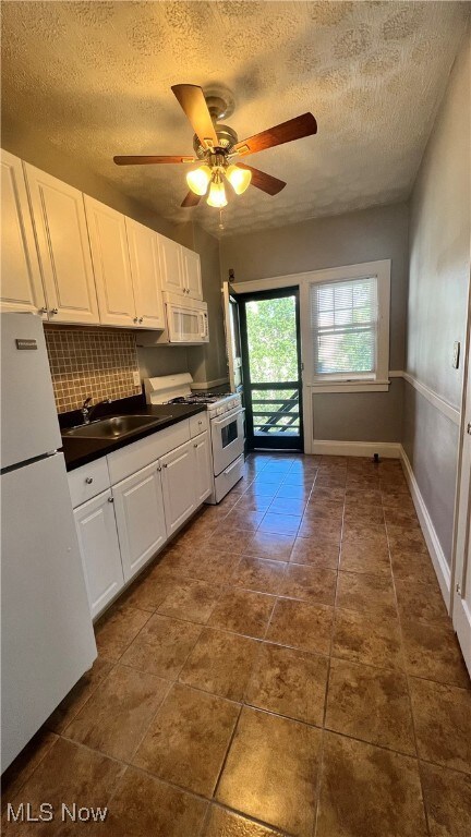 Kitchen with dark countertops, white cabinetry, white appliances, backsplash, and a textured ceiling