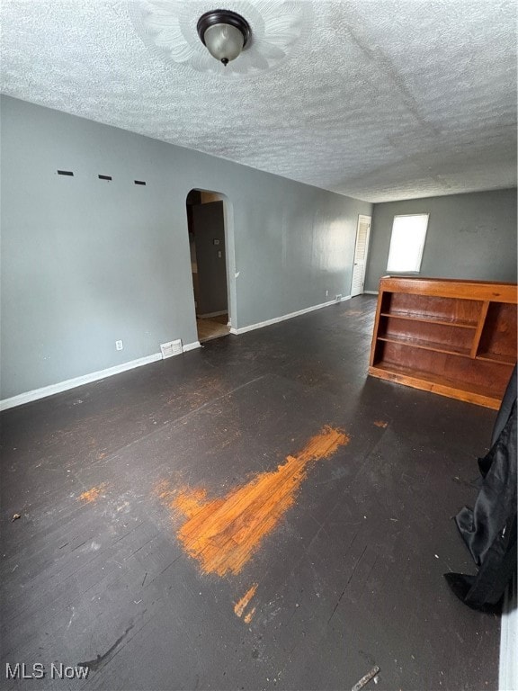 Unfurnished room featuring arched walkways, a textured ceiling, and dark wood finished floors
