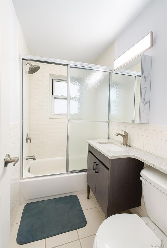 Bathroom with vanity, light tile patterned floors, and shower / bath combination with glass door