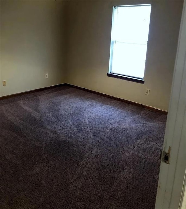Spare room featuring dark colored carpet and baseboards