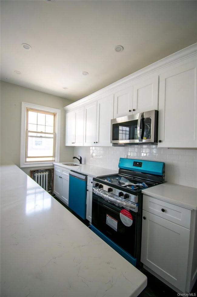 Kitchen featuring stainless steel appliances, tasteful backsplash, white cabinets, radiator heating unit, and recessed lighting