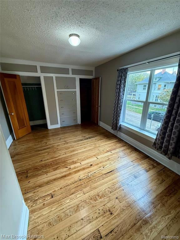 Primary bedroom with multiple closets, a textured ceiling, and light wood floors