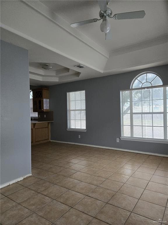 Empty room featuring ceiling fan, a raised ceiling, and light tile patterned floors