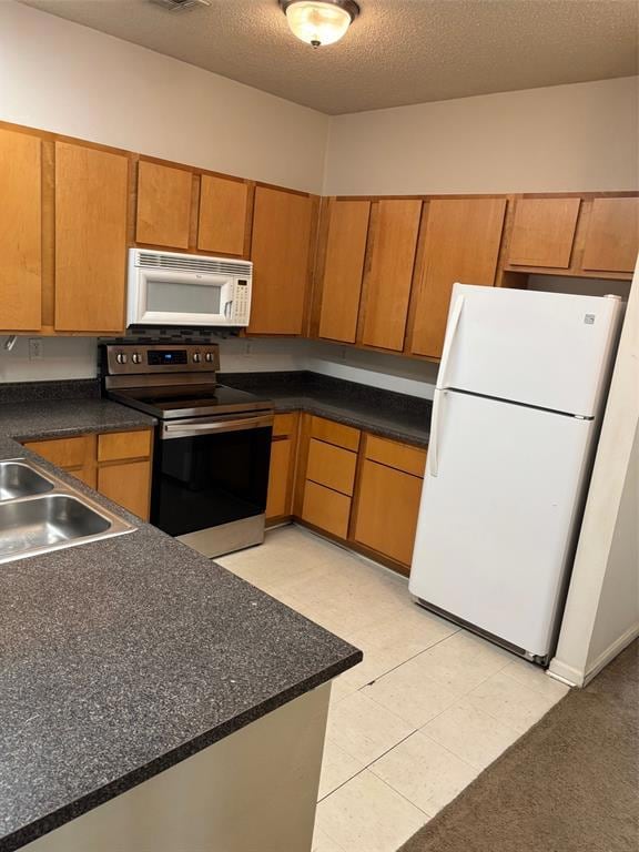 Kitchen featuring refrigerator, stove, brown cabinets, dark countertops, and a textured ceiling