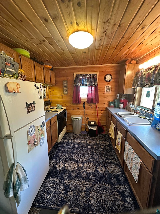 Kitchen with white appliances, wood ceiling, brown cabinets, a sink, and wooden walls
