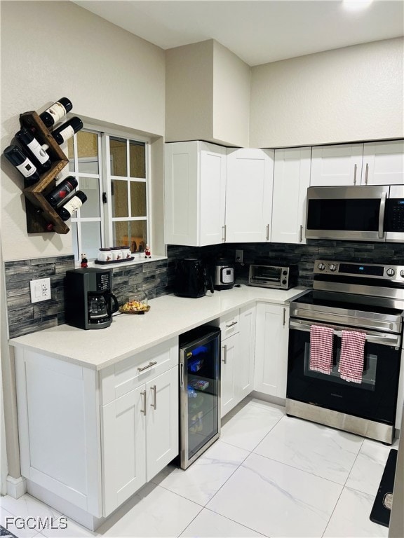 Kitchen with backsplash, appliances with stainless steel finishes, white cabinets, beverage cooler, and light stone countertops