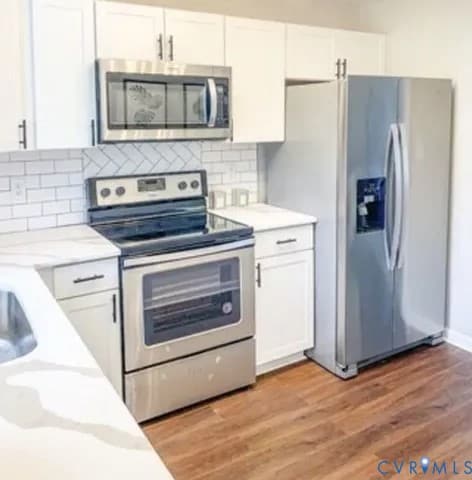 Kitchen with appliances with stainless steel finishes, white cabinets, light wood-type flooring, and tasteful backsplash