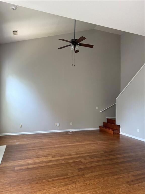 Spare room with a ceiling fan, lofted ceiling, wood finished floors, and stairs