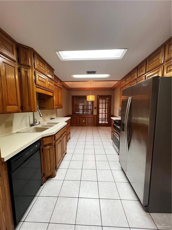 Kitchen with fridge, dishwashing machine, light tile patterned flooring, light countertops, and brown cabinetry