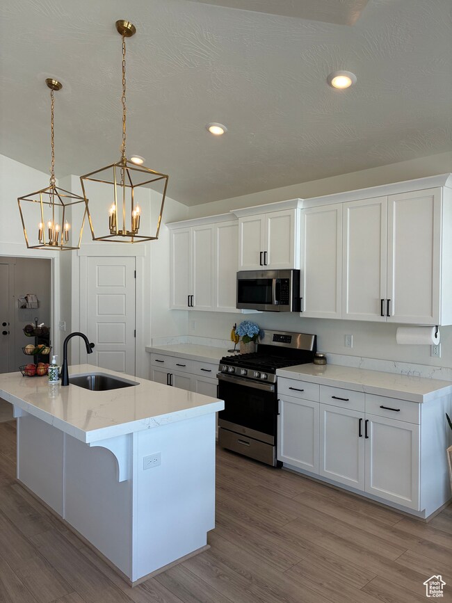 Kitchen with appliances with stainless steel finishes, white cabinets, a breakfast bar, light wood finished floors, and recessed lighting
