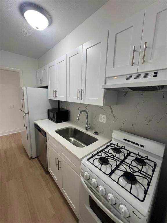 Kitchen with white gas range oven, under cabinet range hood, stainless steel dishwasher, black microwave, and a sink