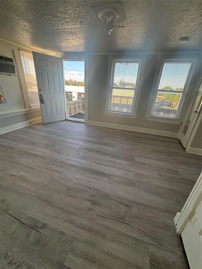 Unfurnished dining area with a wall unit AC, hardwood / wood-style flooring, a textured ceiling, and a wealth of natural light