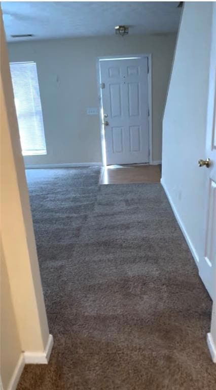 Foyer featuring baseboards and dark carpet