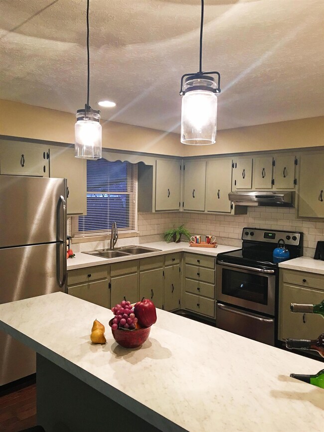 Raised breakfast counter overlooks extra counter space and L-shaped kitchen beyond. Pendant lights compliment cabinet hardware.