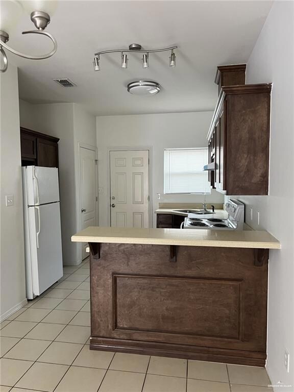 Kitchen featuring freestanding refrigerator, electric stove, a peninsula, and dark brown cabinetry