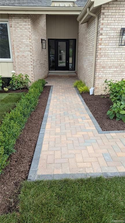 Doorway to property featuring roof with shingles and brick siding