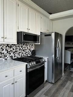 Kitchen with stainless steel appliances, light wood-style floors, tasteful backsplash, white cabinetry, and crown molding