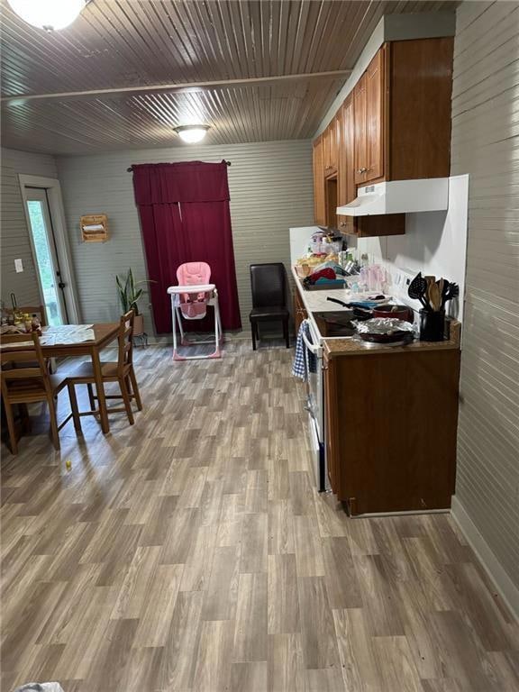 Kitchen featuring range with electric stovetop, wooden walls, light wood-type flooring, under cabinet range hood, and brown cabinets