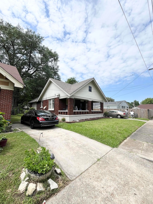 View of front of home with brick siding, concrete driveway, a front yard, and covered porch