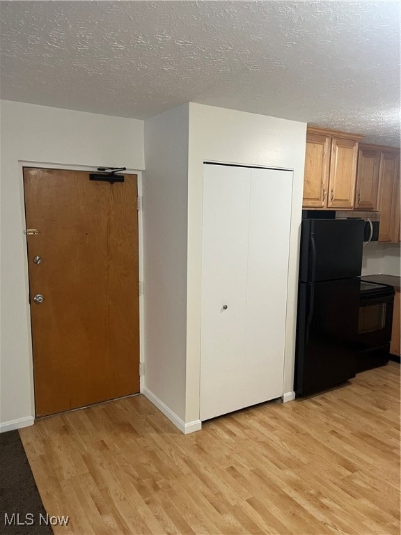 Kitchen featuring light wood-style floors, fridge, a textured ceiling, range, and brown cabinetry