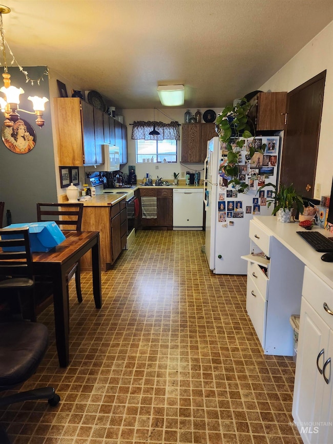 Kitchen with white appliances, tile patterned floors, light countertops, a chandelier, and decorative light fixtures
