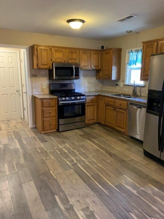 Kitchen with wood cabinets, dw, 5 burner gas stove, microwave with vent less hood and window looking out to street.