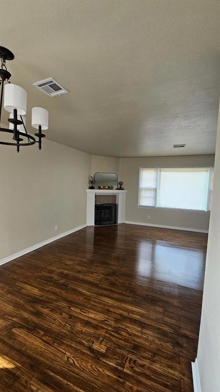 Unfurnished living room featuring dark wood-style floors, a fireplace, a textured ceiling, and a chandelier