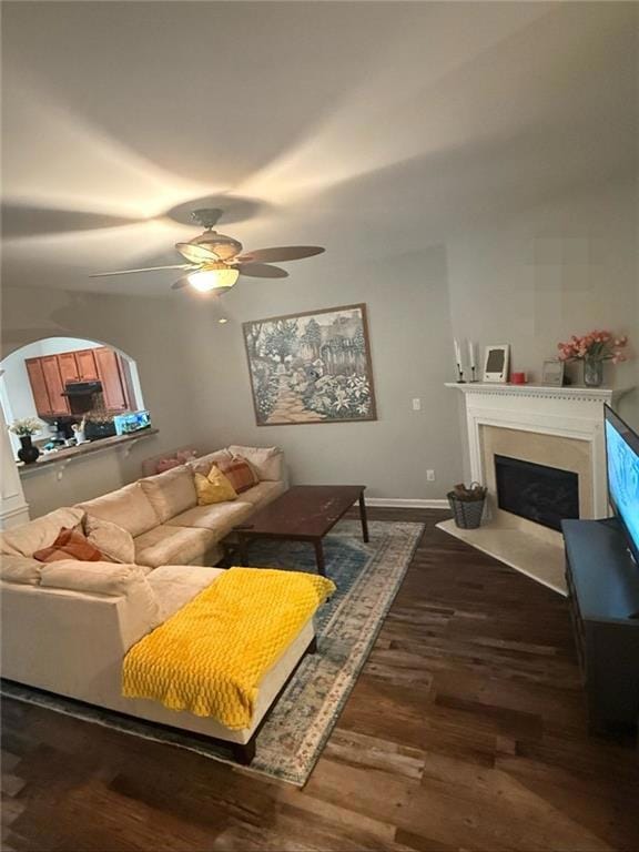 Living area featuring a fireplace with flush hearth, ceiling fan, and dark wood-type flooring