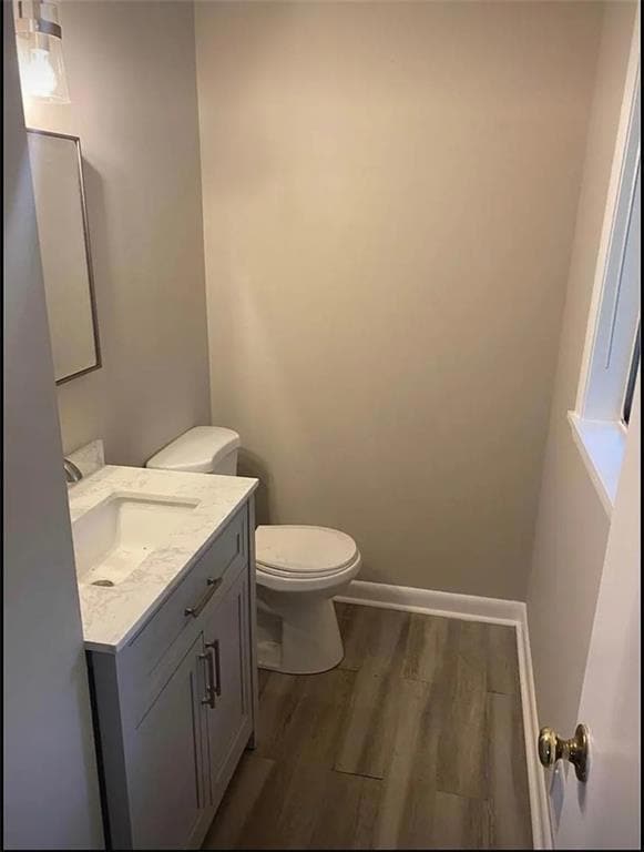 Half bath featuring vanity, wood finished floors, toilet, and baseboards