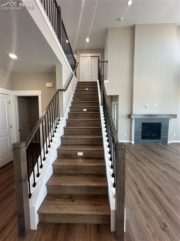 Stairs with a tile fireplace, wood finished floors, recessed lighting, and a textured ceiling