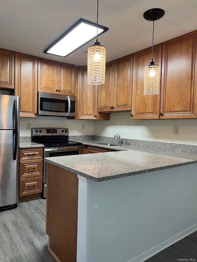 Kitchen with brown cabinets, dark wood finished floors, appliances with stainless steel finishes, and a peninsula