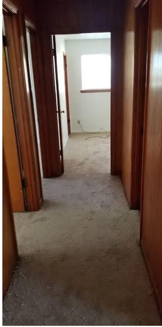 This photo shows a narrow, carpeted hallway with w