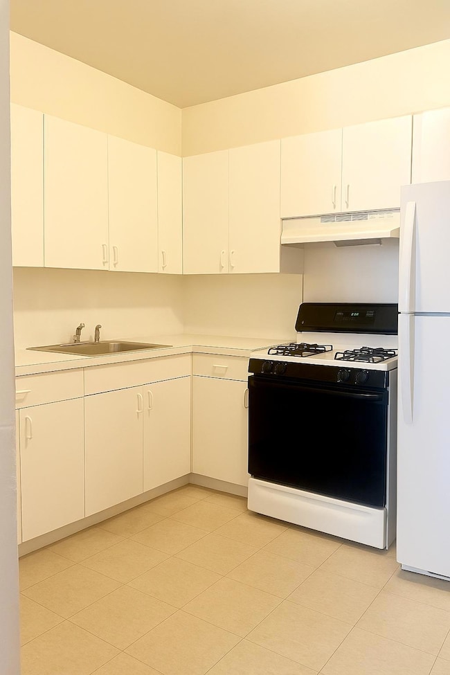 Kitchen featuring range with gas cooktop, freestanding refrigerator, under cabinet range hood, and light countertops