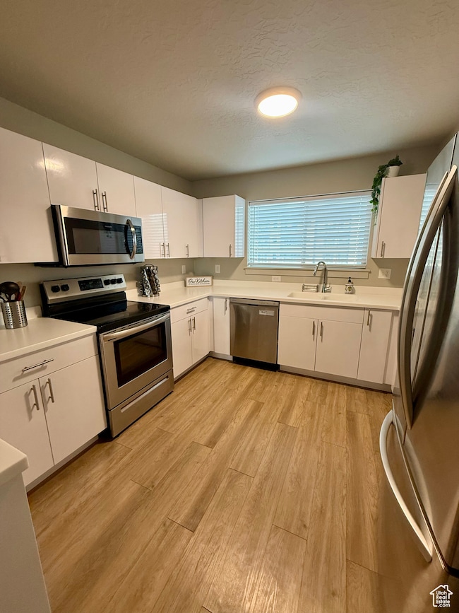 Kitchen featuring white cabinetry, stainless steel appliances, light countertops, light wood-style flooring, and a textured ceiling
