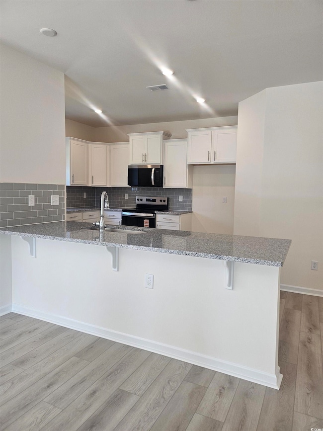 Kitchen featuring a kitchen bar, light stone counters, white cabinetry, decorative backsplash, and appliances with stainless steel finishes Please note photos are of similar home plan, colors and options vary from home