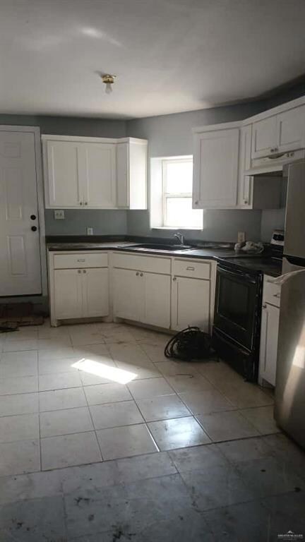 Kitchen featuring white cabinets, black / electric stove, dark countertops, freestanding refrigerator, and light tile patterned flooring