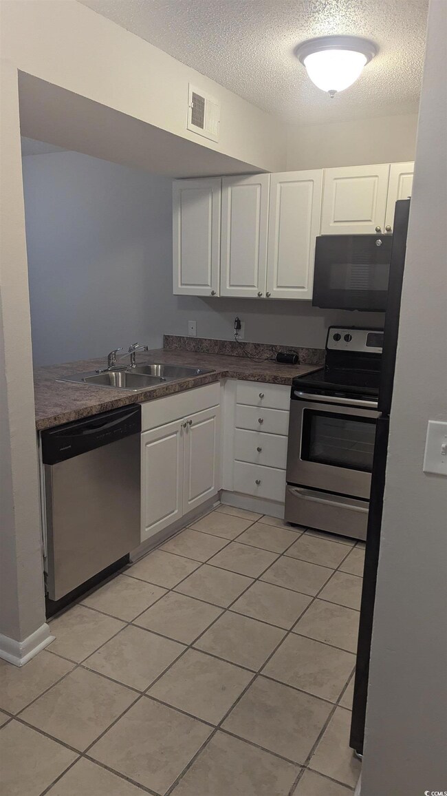 Kitchen featuring appliances with stainless steel finishes, a sink, white cabinetry, a textured ceiling, and light tile patterned floors