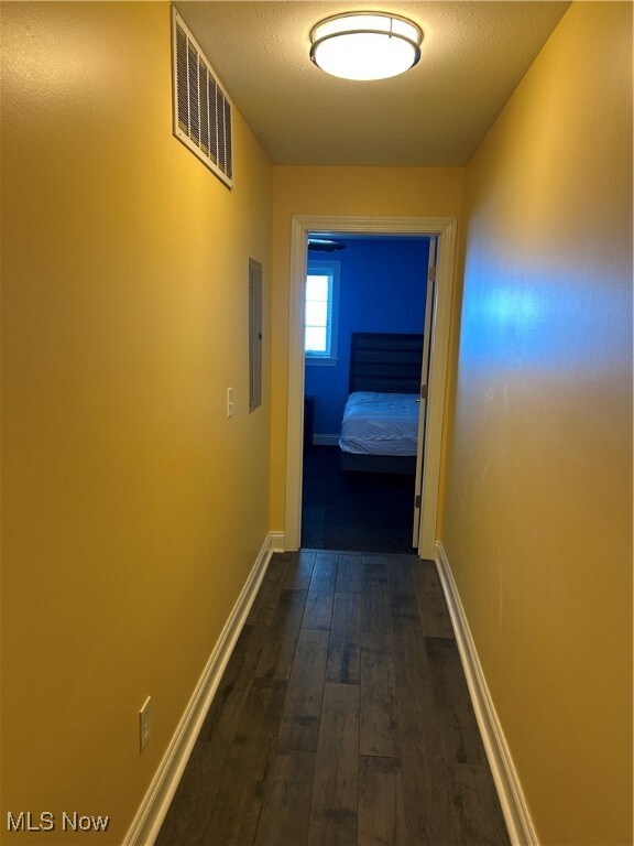 Hall featuring visible vents, baseboards, electric panel, a textured ceiling, and dark wood-type flooring