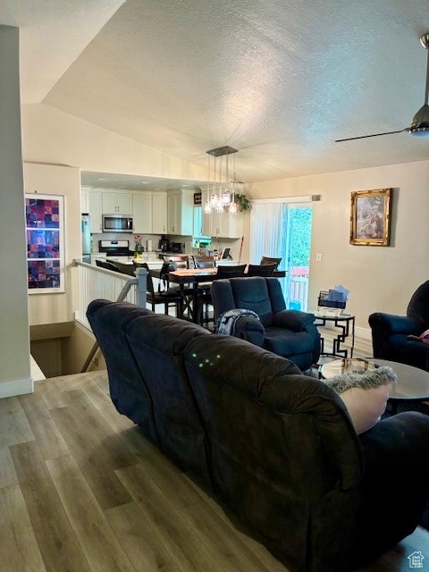 Living room featuring light wood-type flooring, vaulted ceiling, a textured ceiling, and a chandelier