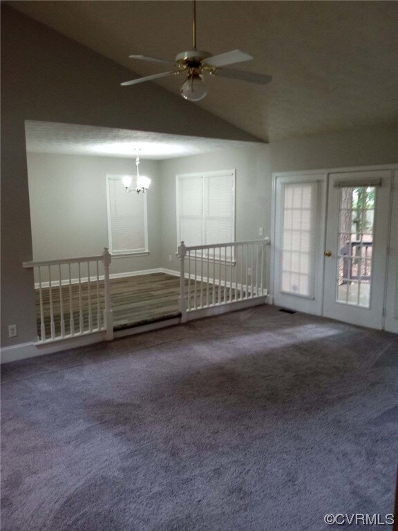 Carpeted spare room featuring vaulted ceiling and ceiling fan with notable chandelier