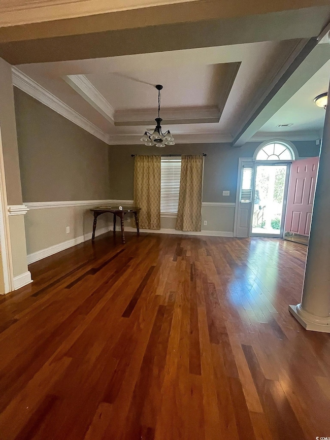 Dining Area featuring a tray ceiling, dark wood finished floors, a chandelier, and ornamental molding