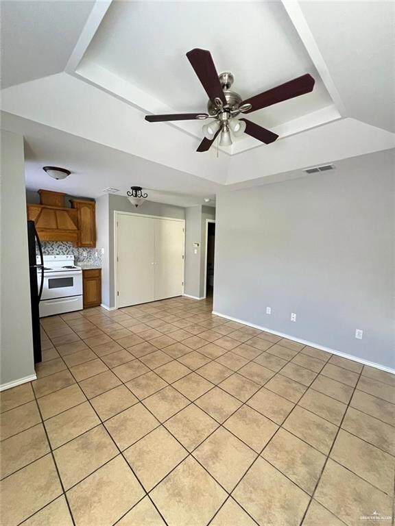 Unfurnished living room with a tray ceiling, light tile patterned floors, and ceiling fan