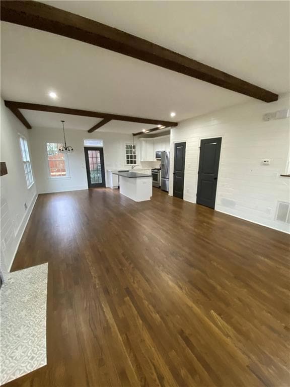 Unfurnished living room featuring beam ceiling, dark wood finished floors, a chandelier, and recessed lighting