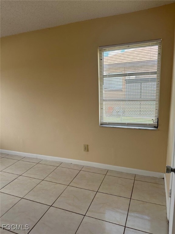 Empty room with a textured ceiling and light tile patterned flooring