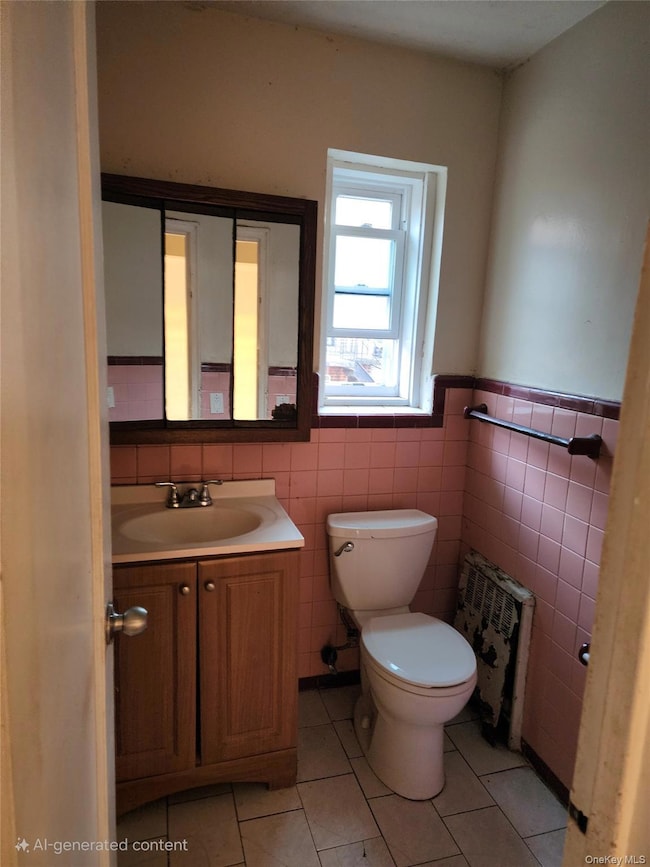 Bathroom with light tile patterned floors, vanity, radiator heating unit, tile walls, and a wainscoted wall