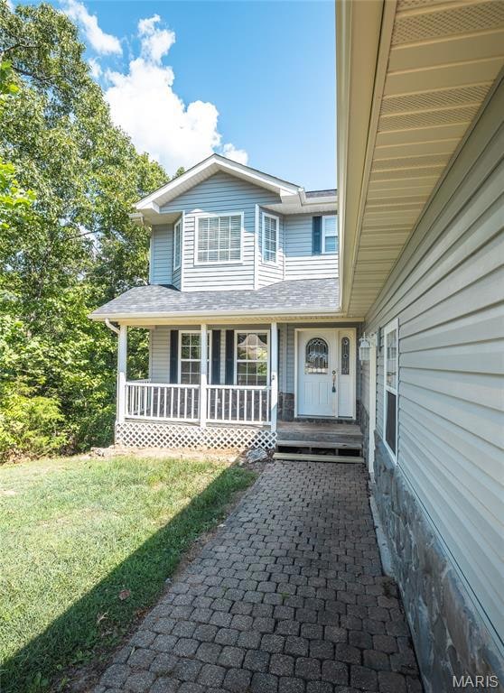 Property entrance featuring covered porch, a yard, and a shingled roof