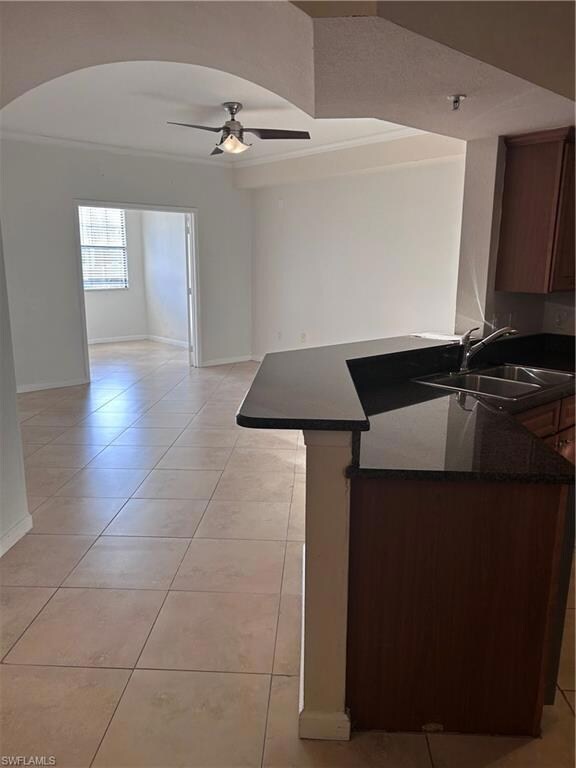 Kitchen with light tile patterned floors, ceiling fan, a peninsula, crown molding, and dark stone counters