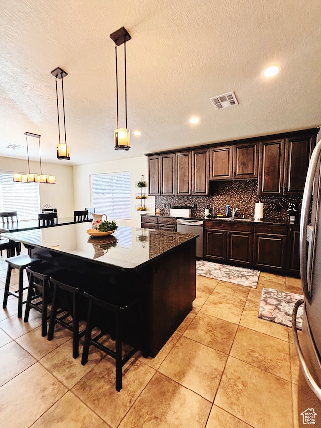 Kitchen with stainless steel dishwasher, decorative backsplash, a textured ceiling, a center island, and light tile patterned floors