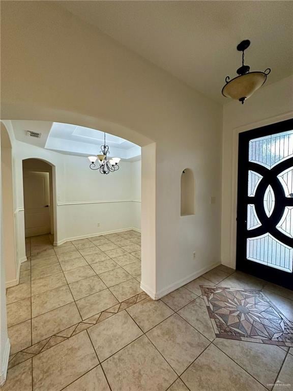 Foyer entrance featuring a chandelier, light tile patterned floors, arched walkways, and baseboards